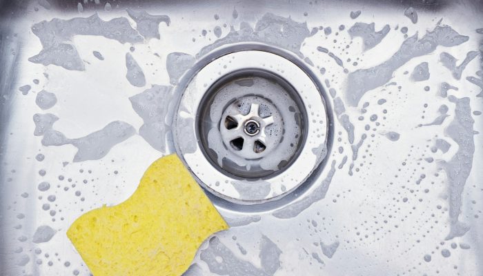 Closeup sink drain and yellow sponge. Cleaning metallic sink housework concept